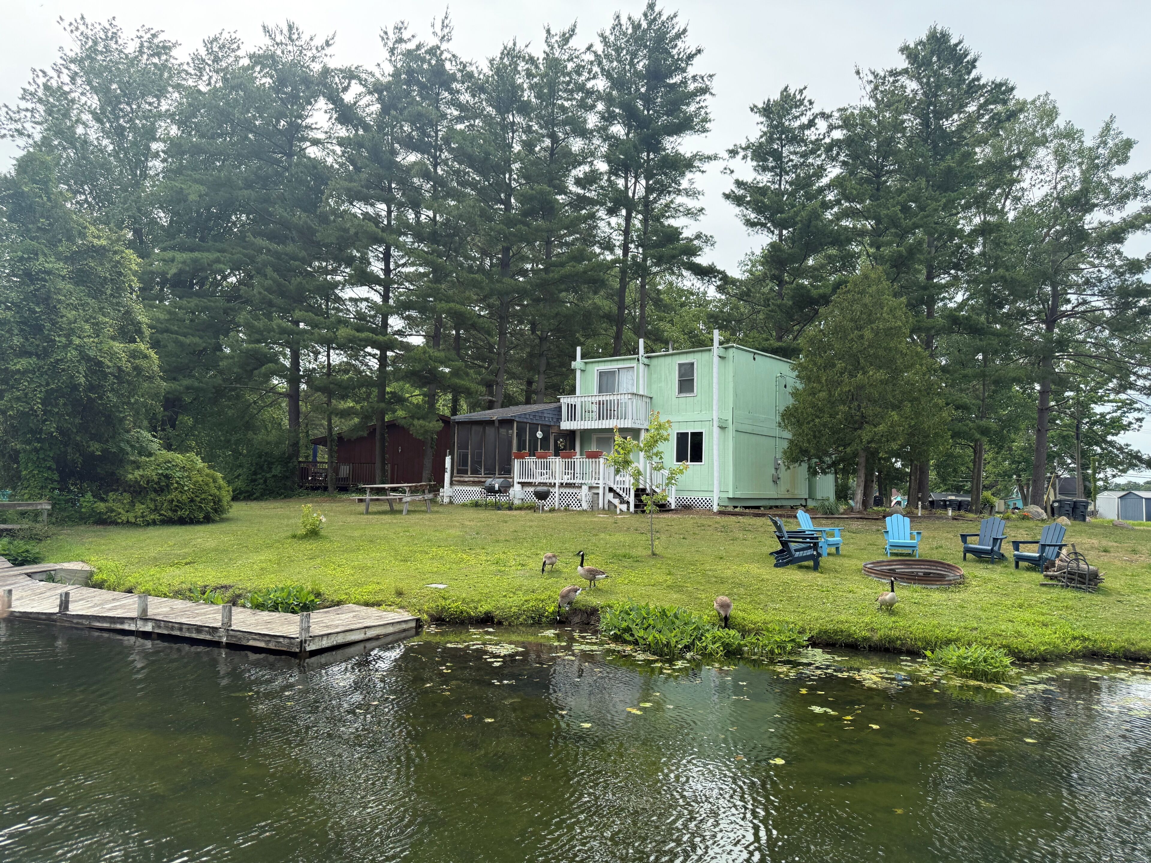 A lakeside cabin with a dock, surrounded by trees and a grassy area with outdoor seating.