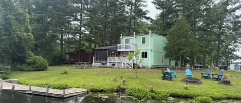 A lakeside cabin with a dock, surrounded by trees and a grassy area with outdoor seating.