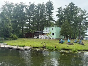 A lakeside cabin with a dock, surrounded by trees and a grassy area with outdoor seating.