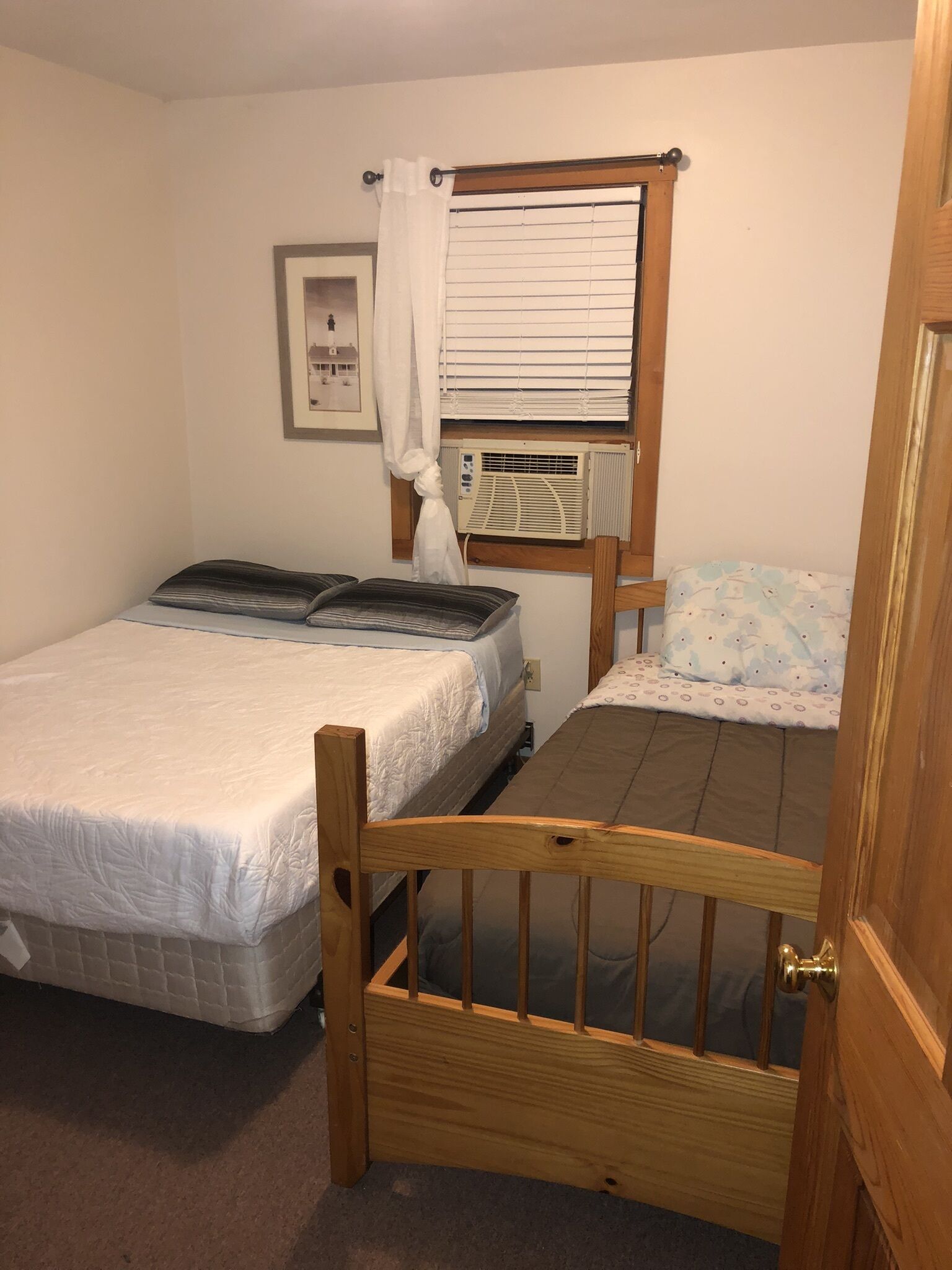 A small, single-room accommodation with two beds, a window with blinds, a radiator, and a door.