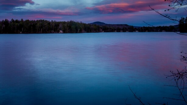 A calm lake with a forested shoreline and a mountain in the background.