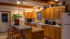 A kitchen with wooden cabinets, a central island with stools, a potted plant, and a refrigerator.