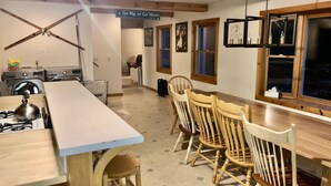 A kitchen with a central island, wooden chairs, a dining table, and a view of the outside through windows.