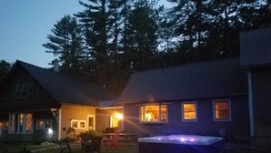 A house with a hot tub in the yard, a covered patio, and a large tree in the background.
