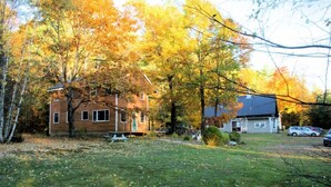 A wooden house surrounded by autumn foliage, with a grassy yard and a picnic table.