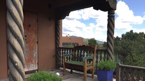 A wooden porch with a bench, two potted plants, and a view of the surrounding landscape. - Authentic Santa Fe Casita with Views on the Edge of Town (Santa Fe)