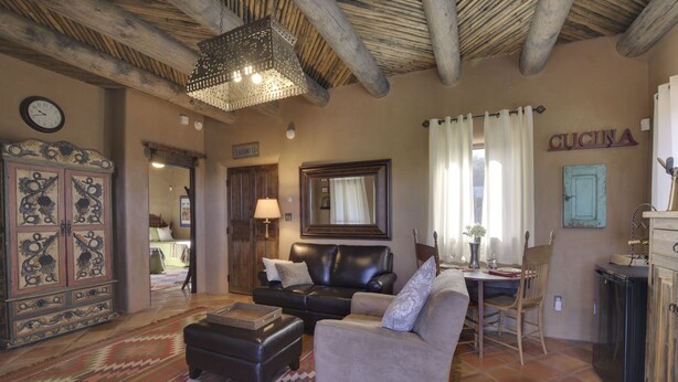 A cozy living room with a sofa, ottoman, and a dining area with a table and chairs. A kitchen area with a sink and cabinets is visible. - Authentic Santa Fe Casita with Views on the Edge of Town (Santa Fe)