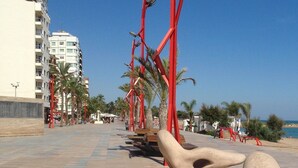 Une promenade agrémentée d’éléments architecturaux rouges, de palmiers et, au loin, d’une plage.