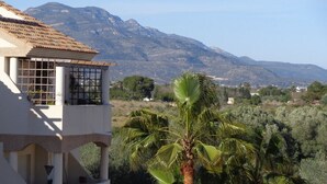 Un bâtiment blanc, doté d’un toit en tuiles et de grandes fenêtres, qui offre une vue sur un paysage montagneux et des palmiers.