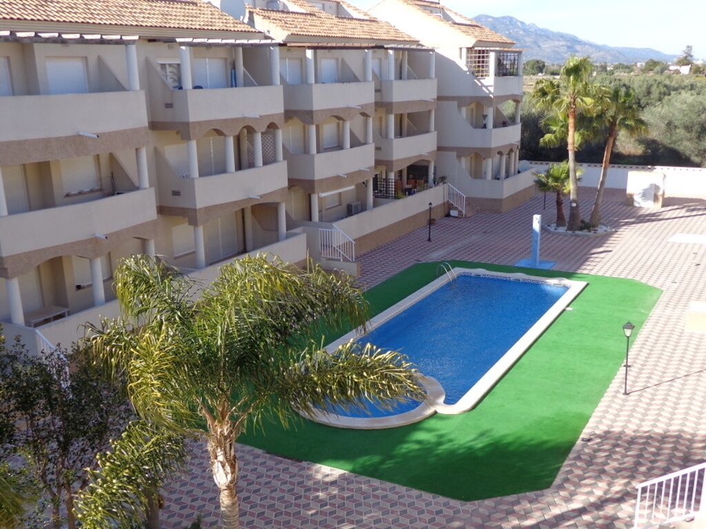 Ein mehrstöckiges Hotel mit Balkonen, einem Schwimmbad und Palmen.