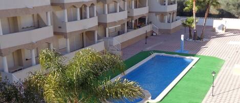 Ein mehrstöckiges Hotel mit Balkonen, einem Schwimmbad und Palmen.