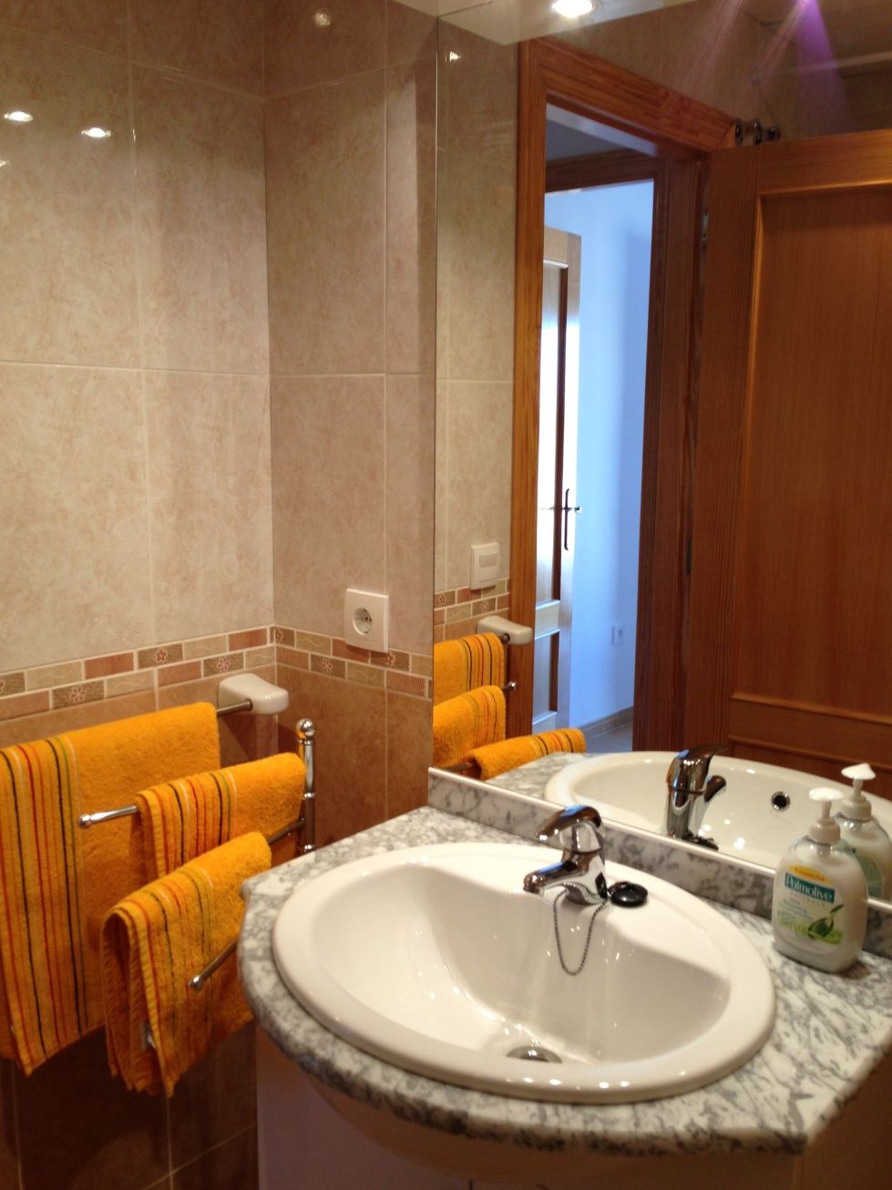 A bathroom with two sinks, a large mirror, and orange towels.