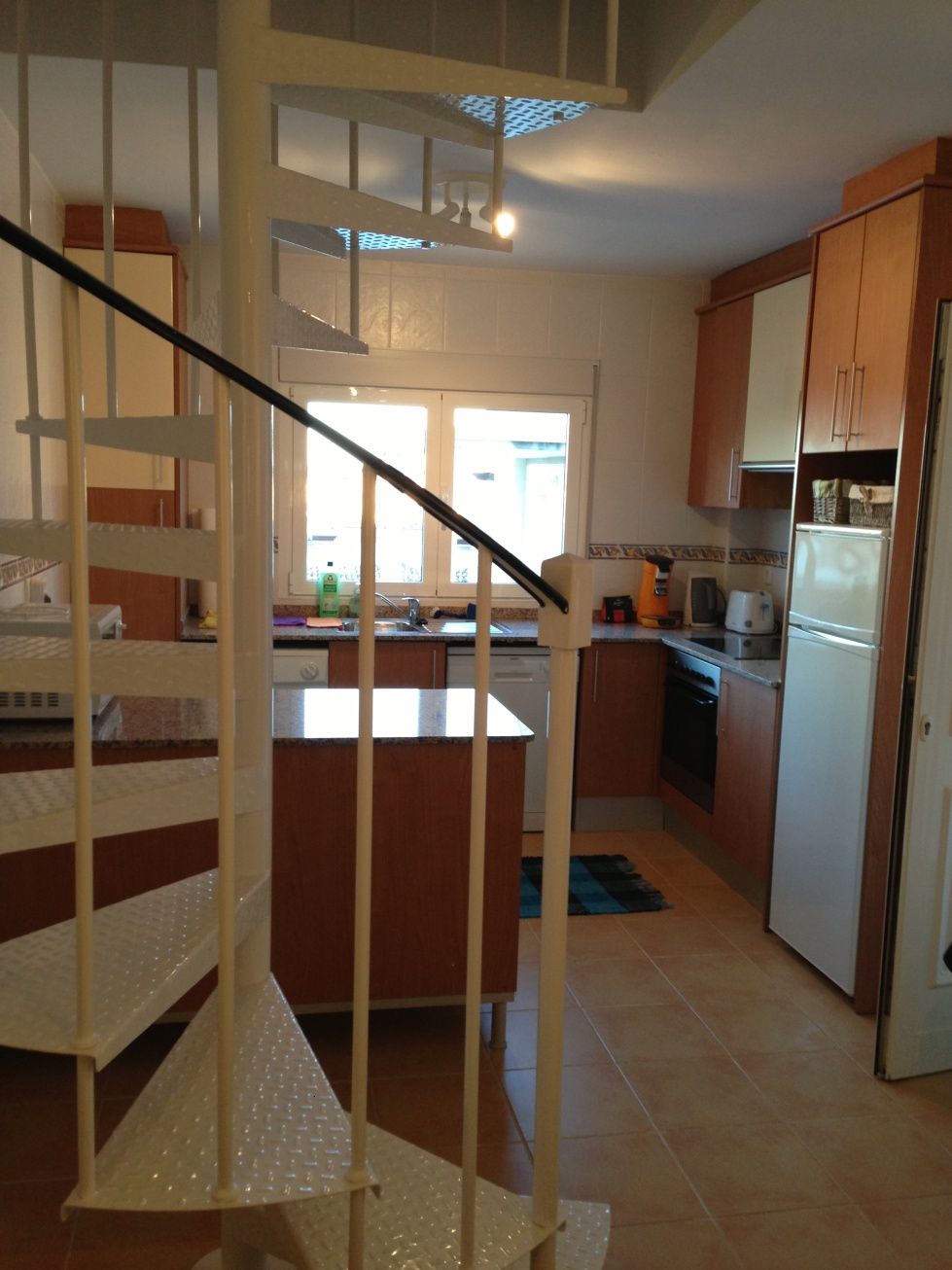 A kitchen with wooden cabinets, a built-in oven, a refrigerator, and a staircase with a handrail.