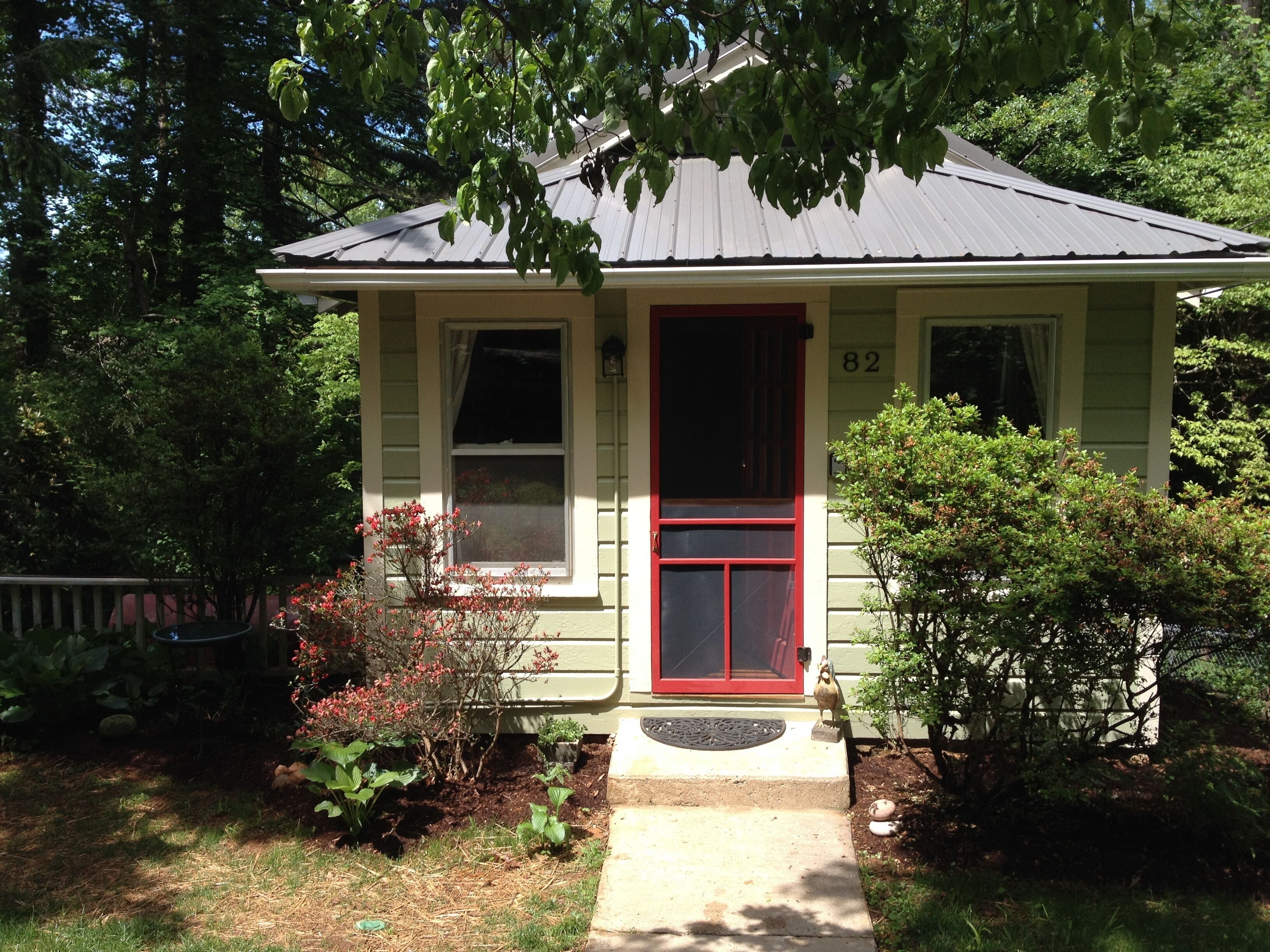 A small, single-story house with a red door and a number '82' on the front wall.