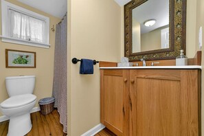 Une salle de bain comprenant des toilettes, un meuble en bois, un lavabo avec miroir et une fenêtre avec des rideaux.