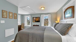 A bedroom with a large bed, a window with curtains, a ceiling light, and framed pictures on the wall. - Dreamy Cottage for Two (Brevard)