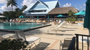 A resort with a swimming pool, lounge chairs, and a thatched-roof building.