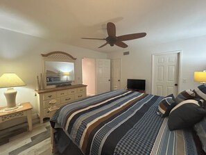 Ein Schlafzimmer mit Bett, Kommode, Spiegel, Deckenventilator, Fernseher und zwei Türen.