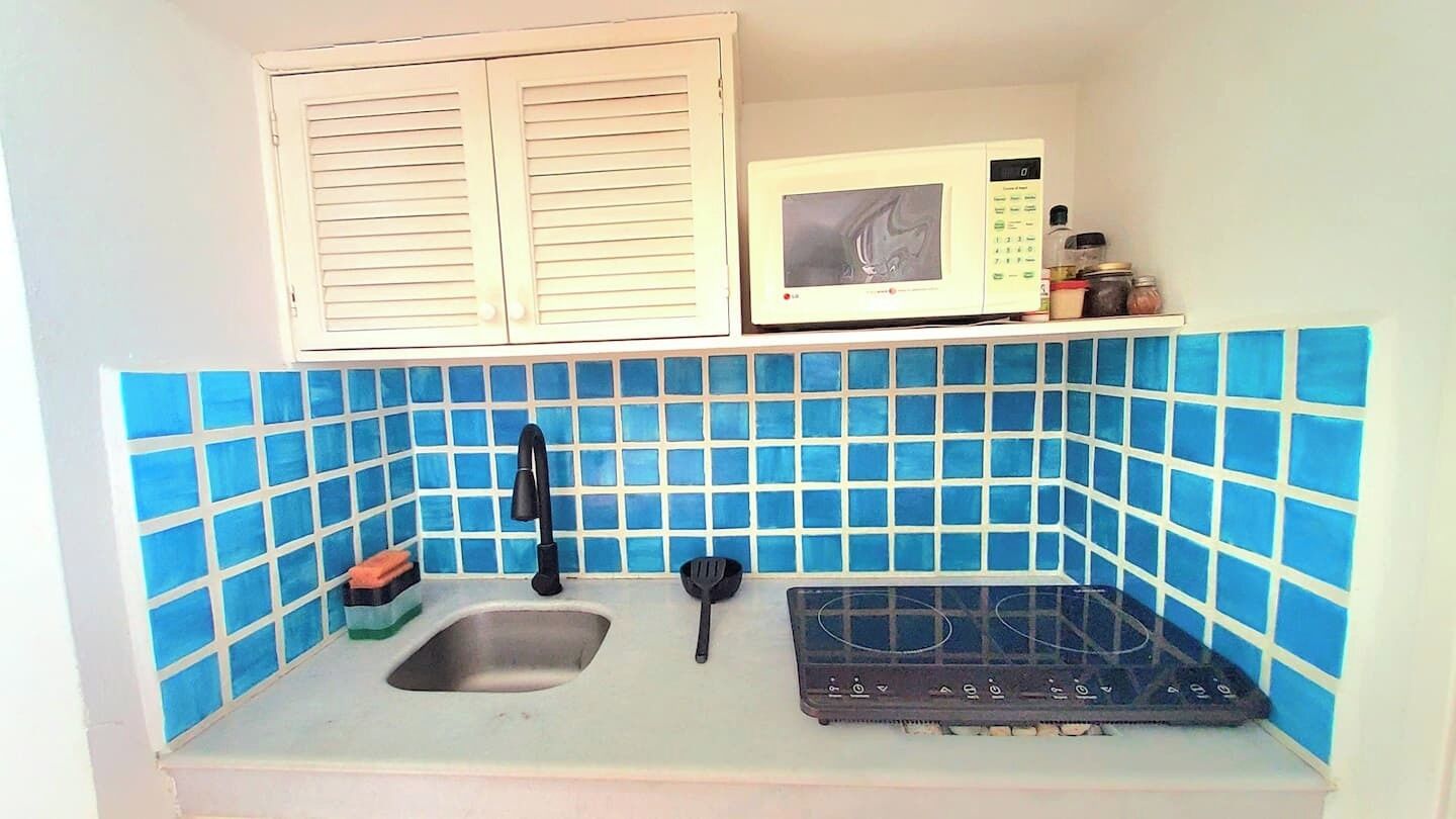 A compact kitchen with a sink, a stove, a microwave, and a window with shutters.