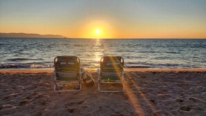 Twee strandstoelen gericht op de oceaan, met een ondergaande zon op de achtergrond.
