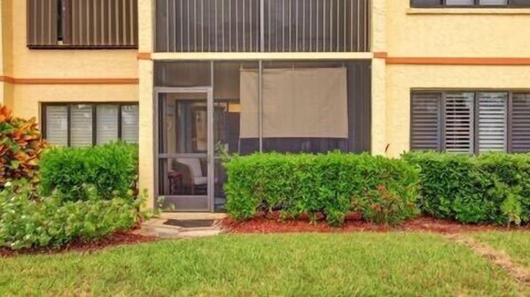 A modern building with a glass door entrance, a small outdoor seating area, and neatly trimmed hedges.
