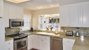 A modern kitchen with white cabinets, stainless steel appliances, a granite countertop, and a red patterned rug. - Gathering Place overlooking beach, pier, and downtown Cayucos (Cayucos)