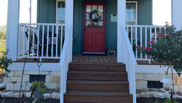 Une maison à deux étages avec une porte d’entrée rouge, des balustrades blanches et un porche avant en bois.