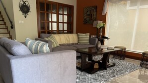 A living room with a grey sofa, a glass coffee table, a patterned rug, and a large window with curtains. - Fabulous Spacious Villa Only Steps Away from the Beach!  (Playa Hermosa)