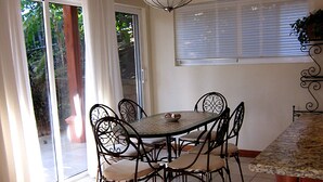 A dining area with a round table and six chairs, a window with blinds, and a view of greenery outside. - Fabulous Spacious Villa Only Steps Away from the Beach!  (Playa Hermosa)