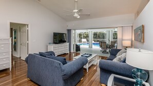 A spacious living room with a ceiling fan, a television, and a pool view. - Tropical Perfection!  3 BR/2 BA & HEATED POOL! Close to beaches, WiFi (Sebastian)