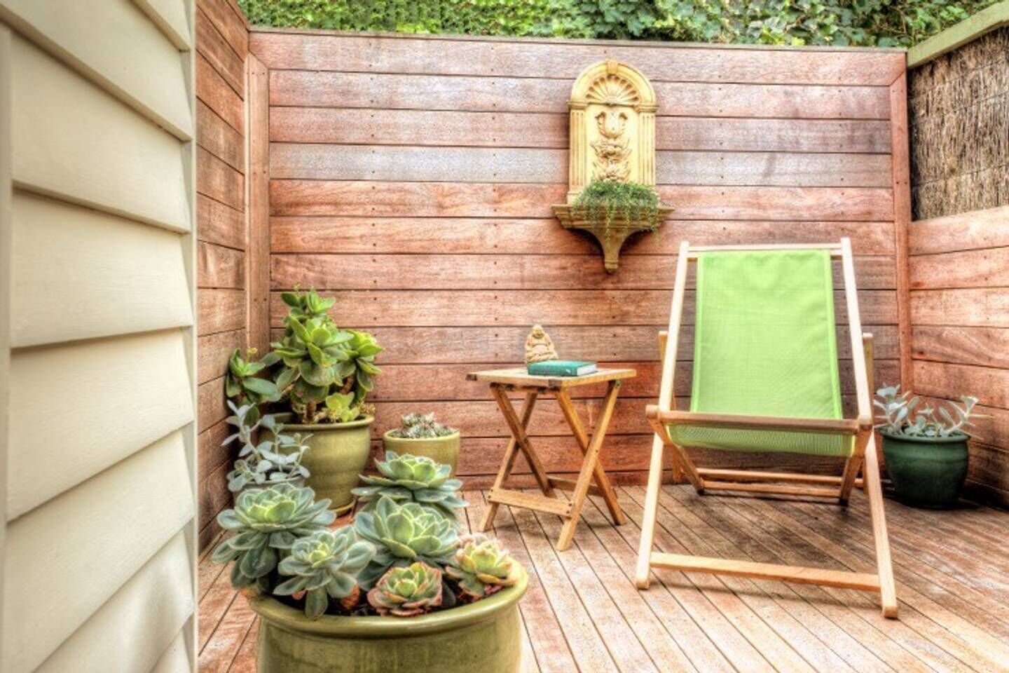 A wooden deck with potted succulents, a small table with a green cloth, and a wooden easel with a green cloth.