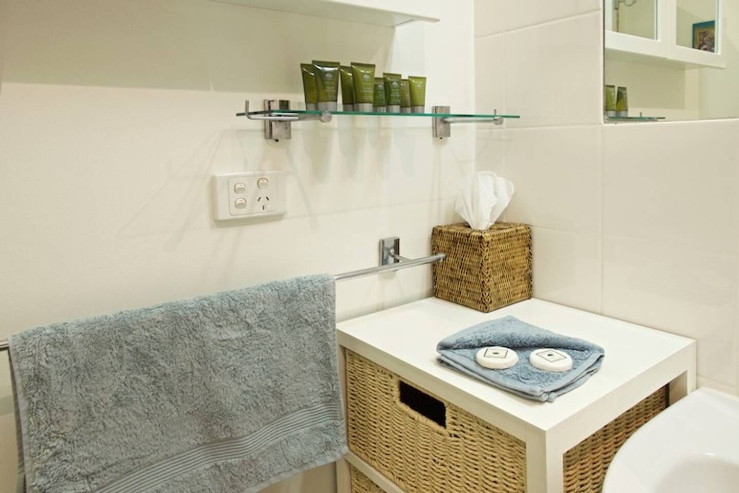 A bathroom with a white sink, a towel rack with a blue towel, a tissue box, and a shelf with toiletries.