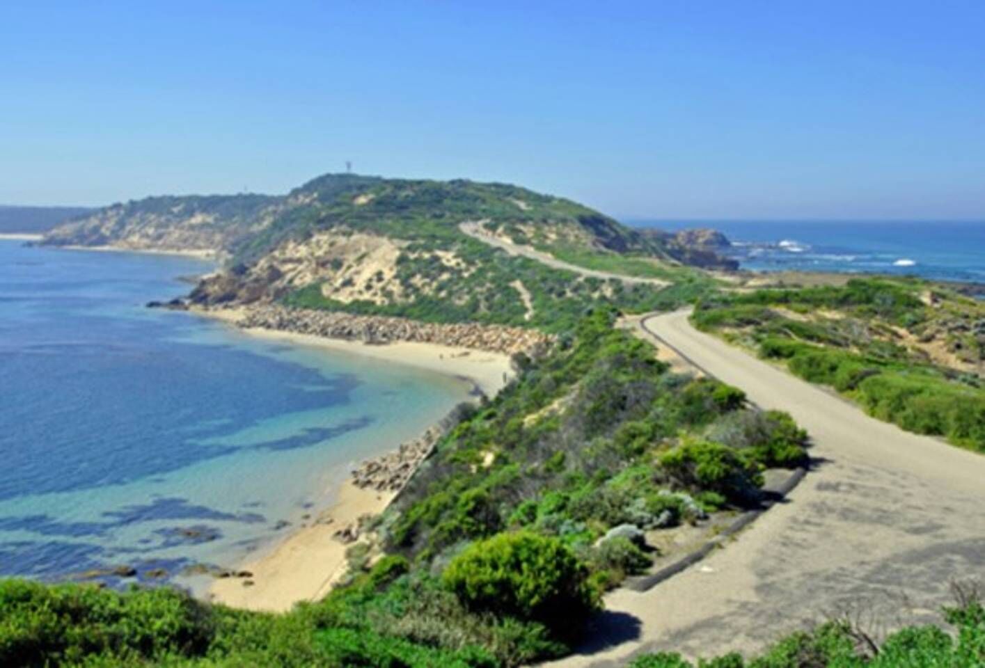 A coastal road with a beach and a hill.