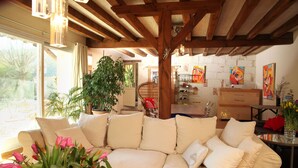 Un salon chaleureux avec un canapé d’angle beige, une grande plante en pot et un coin repas comprenant une table et des chaises en bois.