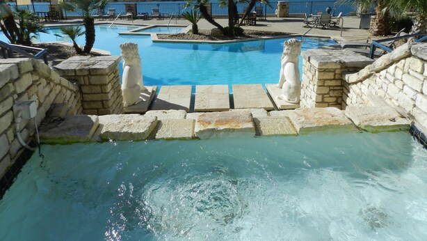 Zona de piscina con escalones de piedra que bajan al agua, rodeada de tumbonas y palmeras.