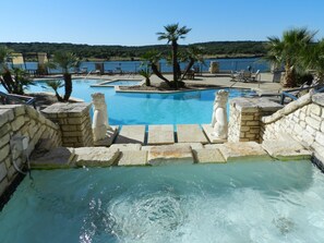 Zona de piscina con escalones de piedra que bajan al agua, rodeada de tumbonas y palmeras.