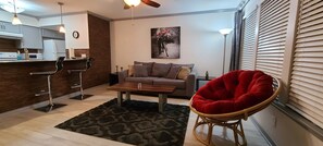 Un salon moderne comprenant un canapé, un fauteuil rouge, une table basse et un coin cuisine avec un comptoir-bar.