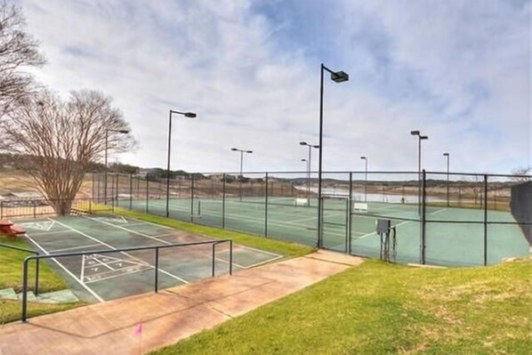 Una cancha de tenis con valla perimetral, una cancha de baloncesto y un sendero para caminar.
