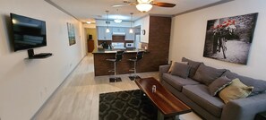 Een moderne woonkamer met een bank, een salontafel, een televisie en een keuken op de achtergrond.