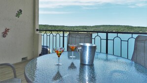 Mesa redonda con una jarra de metal y dos vasos de martini en un balcón con vista a un cuerpo de agua y un paisaje montañoso.
