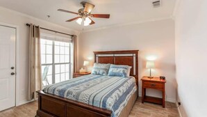 Un dormitorio con cama de madera, ventilador de techo, ventana con cortinas y lámparas de noche.