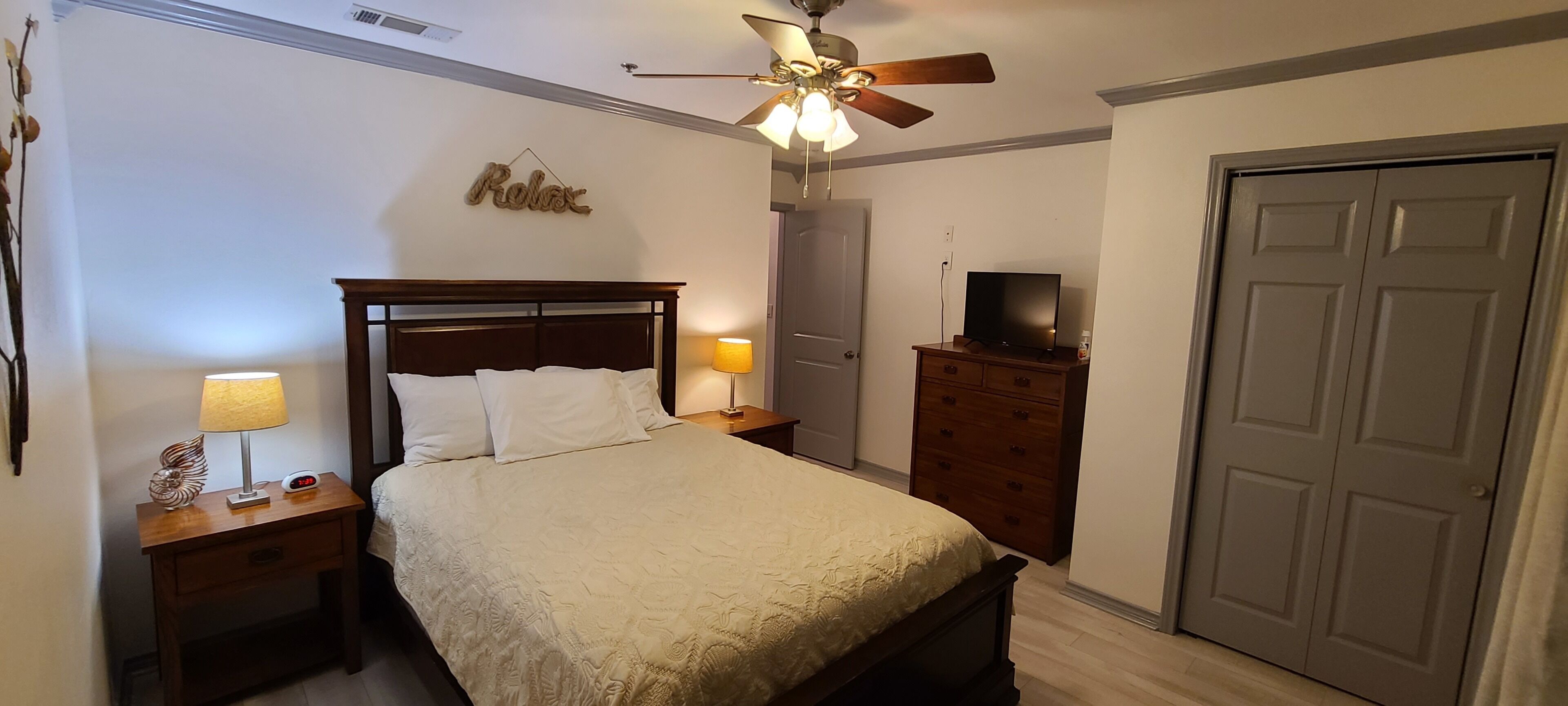 Une chambre à coucher avec un lit, des tables de chevet, une commode, un téléviseur et une porte.
