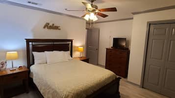 Une chambre à coucher avec un lit, des tables de chevet, une commode, un téléviseur et une porte.