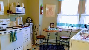 A kitchen with a stove, microwave, and coffee maker. There is a fire extinguisher on the wall and a window with curtains. - Fully equipped apartment for short term vacation rentals! (Calumet)