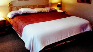 A neatly made bed with a red and white bedspread, a wooden headboard, and a nightstand with a lamp. There are framed pictures on the wall above the bed. - Fully equipped apartment for short term vacation rentals! (Calumet)