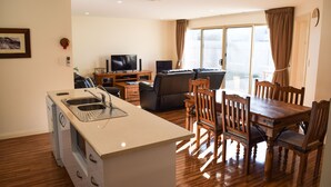 Een moderne woonkamer met een keukeneiland, een eethoek met houten stoelen, een bank en een televisie.