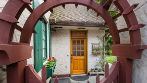 A wooden gate with a circular design, a wooden door, and a small porch area with potted plants.