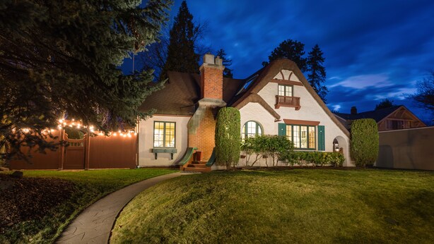 A two-story house with a brick chimney, green shutters, and a wrap-around porch.