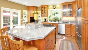 A kitchen with granite countertops, wooden cabinets, a stainless steel refrigerator, and a dining area with chairs.