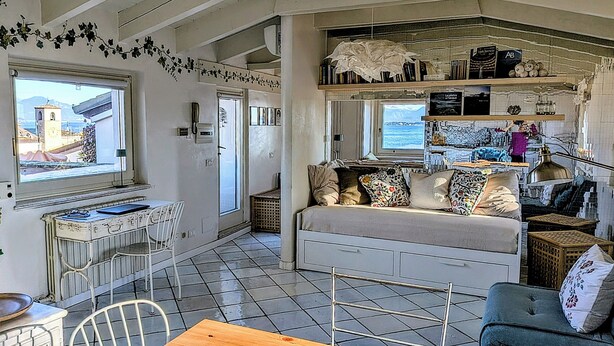 A compact living space with a kitchenette, a sofa, a dining table, and a view of the sea. - Appartment with unique view on the Garda Lake (Desenzano del Garda)